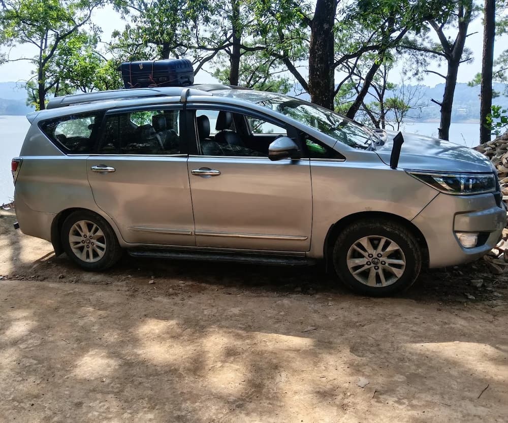 Happy Yatra Travels Innova Crysta parked under the pines by Umiam Lake with luggage on the roof carrier
